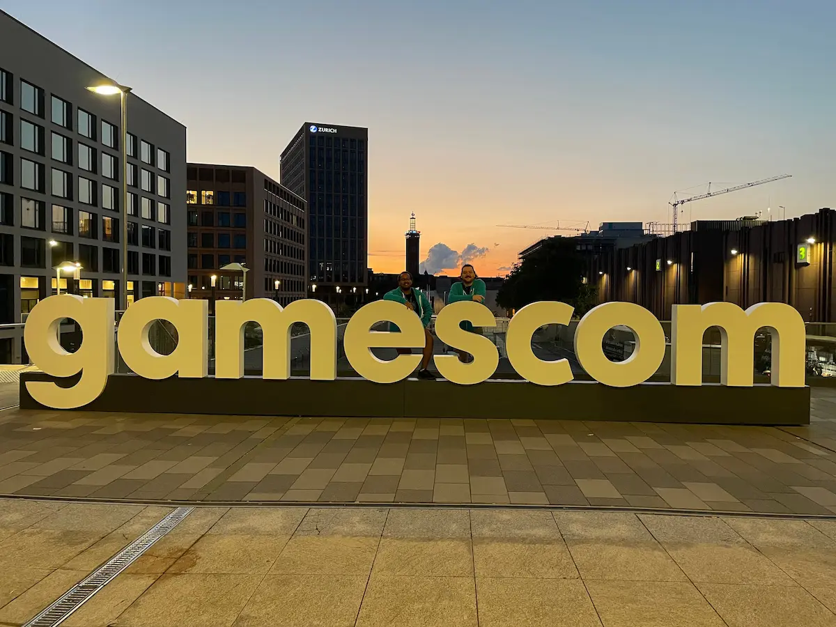 Photo of Mickael and Isael taken in front of the big Gamescom sign at the entrance of the conference centre.
